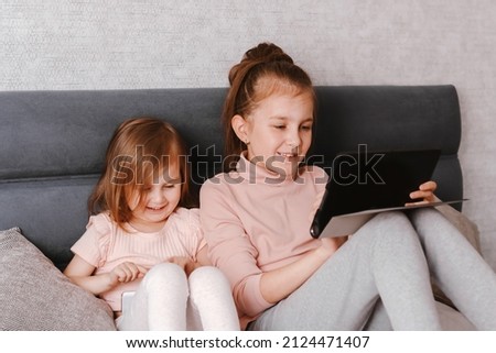 Two little girls sisters holding gadgets, spending time together. Happy children sitting in cozy bedroom and using technologies