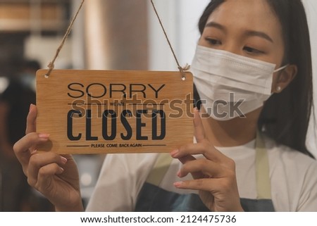 Asian young owner retail,coffee shop woman turning sign board to closed with wearing face mask,protection to pandemic of coronavirus.Close store,restaurant or pub due to lockdown, quarantine of covid.