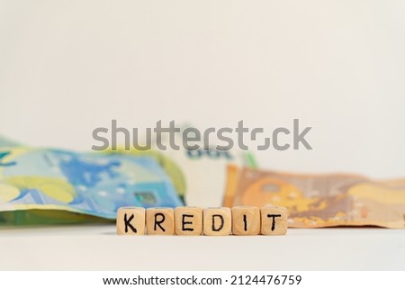 German word for loan, KREDIT, spelled with wooden letters wooden cube on a plain white background with banknotes, concept image 
