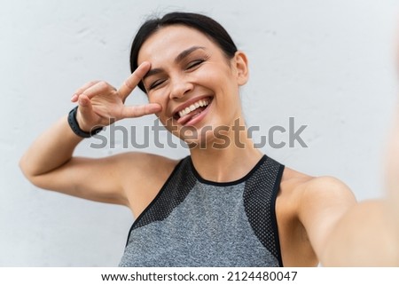 Portrait of smiling playful Caucasian lady making v-sign and sticking out her tongue at camera