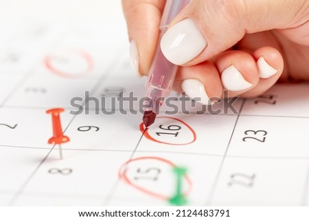 female hand marks with a red marker in the calendar notes an important event several pin marks