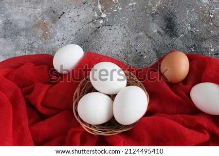 White chicken eggs and one brown egg on a grunge gray background, red fabric, with space for text, copy space, horizontal photo. The concept of the Easter holiday, congratulation, ritual