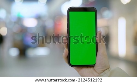 Young woman using smartphone in trade center mall. Female hold mobile phone in hands, text messaging. Person indoors in store with gadget. Electronic technology. Chroma key green screen.