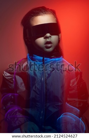 blur portrait cyberpunk boy child in vr glasses in blue and red tones with wires on a red background. Game, virtual reality. Future technologies.
