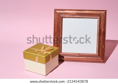 Mockup of wooden frame and Gift box decorated with golden bow on pink background copy space. Minimalist retro style. Template.  mock up holiday. 