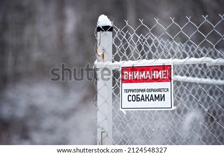 A sign on the fence with the Russian inscription "Attention! The territory is guarded by dogs"