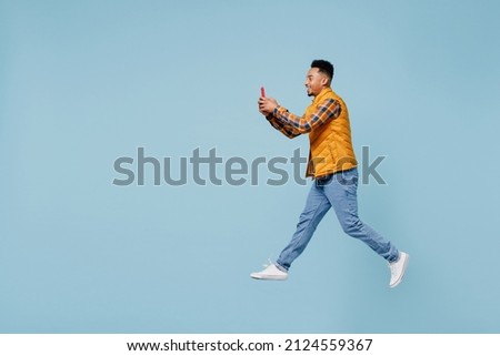 Full size body length side profile view vivid young black man 20s years old wears yellow waistcoat shirt jump hold use mobile cell phone isolated on plain pastel light blue background studio portrait