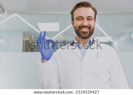Young caucasian confident satisfied positive smiling happy dentist doctor man 30s show ok okay gesture at dental office indoor light modern cabinet near stomatologist Healthcare oral enamel treatment