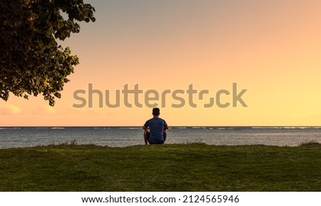 Young man sitting looking out to the ocean. People relaxing, enjoying peace in nature  Royalty-Free Stock Photo #2124565946