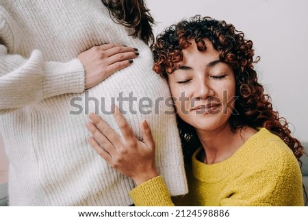LGBT lesbian pregnant woman having tender moment listening her wife baby belly - Focus on right female Royalty-Free Stock Photo #2124598886