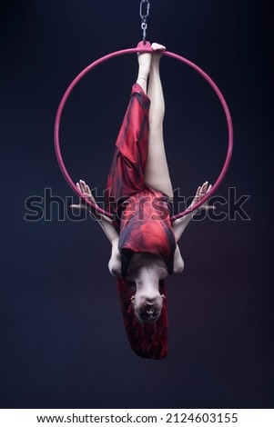 Circus performer woman in red dress doing tricks on red Lyra isolated on black background. Royalty-Free Stock Photo #2124603155
