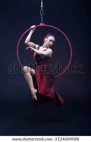 Circus performer woman in red dress doing tricks on red Lyra isolated on black background. Royalty-Free Stock Photo #2124604088