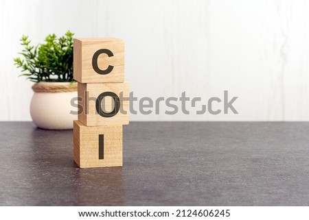 letters of the alphabet of COI on wooden cubes, green plant on a white background. COI - short for Cost of Illness
