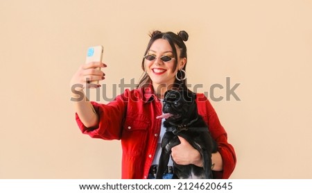 Unusual trendy woman with tattoos poses makes a selfie online life video stream or a photo on a mobile phone with her pet dog, a black pug
