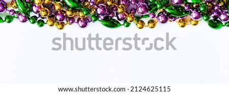 Mardi Gras background. Multicolored beads on white background. Fat Tuesday symbol. Festive decorations in gold, green and purple colors for traditional holiday. Copy space, banner format.