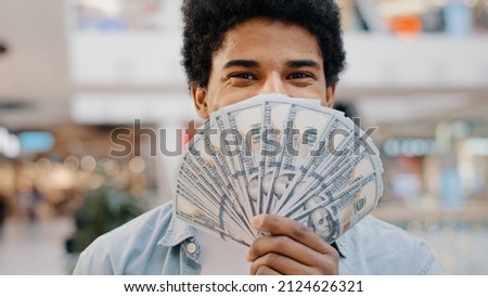 Happy wealthy successful smiling african american business man looking at camera holding fan of money hiding behind dollar banknotes showing financial profit winning salary savings loan credit cash Royalty-Free Stock Photo #2124626321