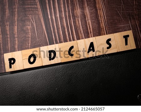 Top view wooden block and notebook with text PODCAST on a wooden background.