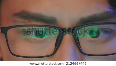 Close Up eyes of a asian man looking at laptop in evening - The light from monitor is reflected on his glasses with stock market investment web