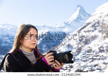Traveler photographer woman with camera taking pictures of landscape of Swiss Alps on sunny winter day ..