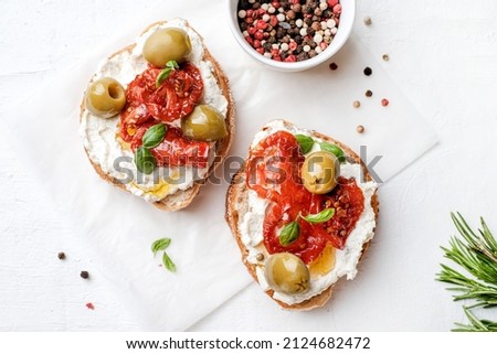 Two bruschettas with ricotta cheese, olive and dried tomatoes on ciabatta bread on white background. Olive oil and spices decorated. Copyspace. Royalty-Free Stock Photo #2124682472
