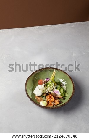 Salad bowl with salmon, avocado, broccoli, vegetables and egg on homemade ceramic plate. Buddha bowl with salmon, broccoli, quinoa in modern serveware. Modern ceramic dishware on concrete background