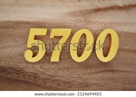Wooden Arabic numerals 5700 painted in gold on a dark brown and white patterned plank background.