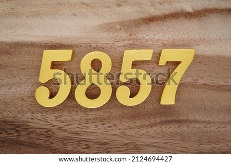 Wooden Arabic numerals 5857 painted in gold on a dark brown and white patterned plank background.