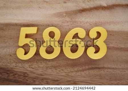 Wooden Arabic numerals 5863 painted in gold on a dark brown and white patterned plank background.