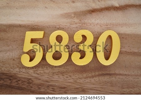 Wooden Arabic numerals 5830 painted in gold on a dark brown and white patterned plank background.