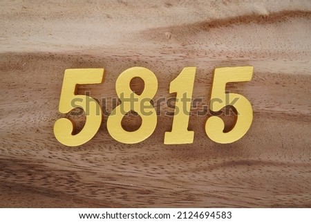 Wooden Arabic numerals 5815 painted in gold on a dark brown and white patterned plank background.