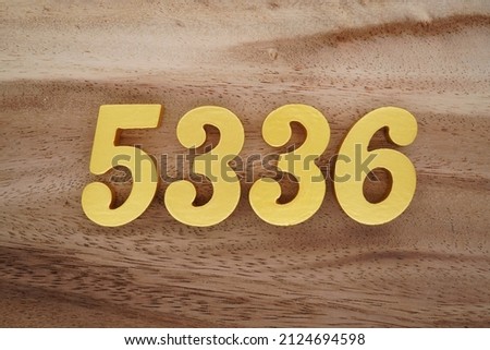 Wooden Arabic numerals 5336 painted in gold on a dark brown and white patterned plank background.
