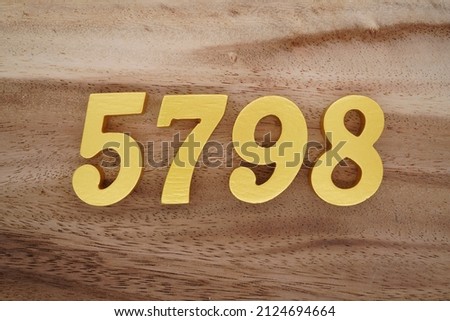 Wooden Arabic numerals 5798 painted in gold on a dark brown and white patterned plank background.