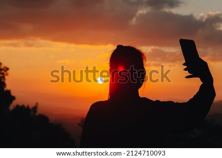 Silhouette of a woman taking a picture in the midst of a beautiful sunset on the mountain.