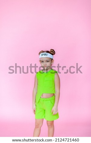 A funny little blonde girl in everyday bright clothes poses alone on a pink studio background. The concept of a child's lifestyle. With a tennis racket.Location of the copy space. Background for your 