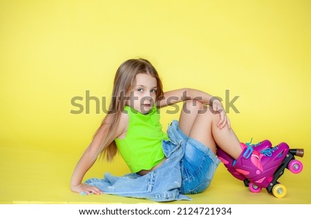 A funny little blonde girl in everyday bright clothes poses alone on a pink studio background. The concept of a child's lifestyle. On roller skates..Location of the copy space. Background for your tex