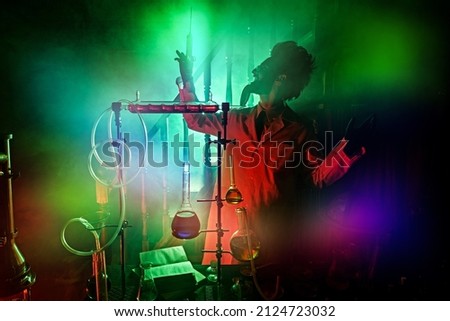 Crazy scientist is working in his laboratory, lit by a mysterious green light and haze. Character of a science fiction novel. Royalty-Free Stock Photo #2124723032