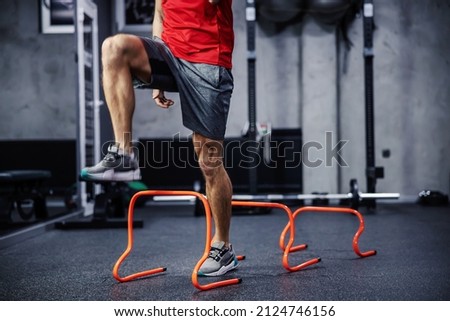 Exercises with hurdles. Close-up shot of a man’s legs in sportswear that skips small hurdles. Jumping over obstacles and warming up for training. Healthy lifestyle, strong movement, dynamism Royalty-Free Stock Photo #2124746156