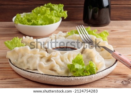 Close-up view of fresh boiled Chinese dumplings on rustic plate with soy sauce and green salad on wooden background. Selective focus. Royalty-Free Stock Photo #2124754283