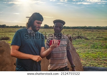Caucasian man using a touch phone with an African man in a village in Botswana