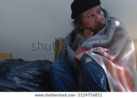 Asian vagrant is siting on the on the sidewalk, wrapped in blanket outdoor Royalty-Free Stock Photo #2124756851