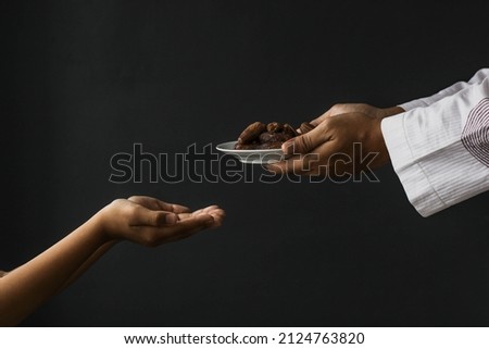 Ramadan kareem concept. Side view Muslim hands giving plate of dates isolated on black background Royalty-Free Stock Photo #2124763820