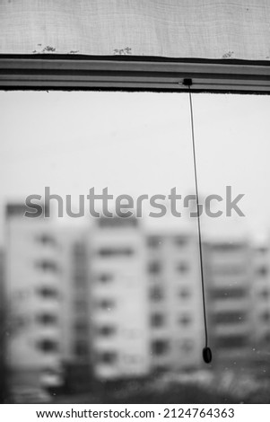 View of the city buildings from the terrace. Half-lowered net and rope swaying in the wind while it snows outside. Black and white photograph.