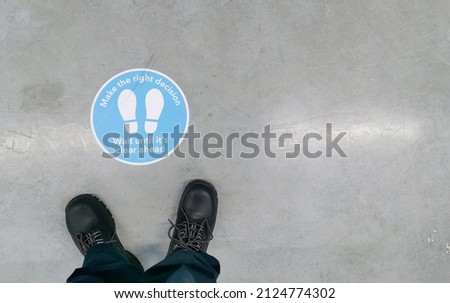Signage to advise on keeping distance seen on the floor of a warehouse with safety boots ahead of it.