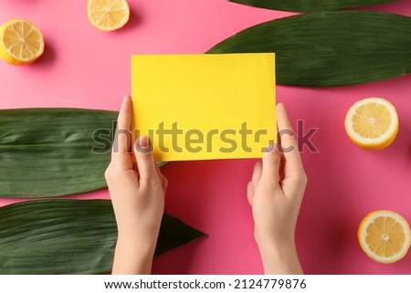 Female hands with blank card, plant leaves and lemons on color background