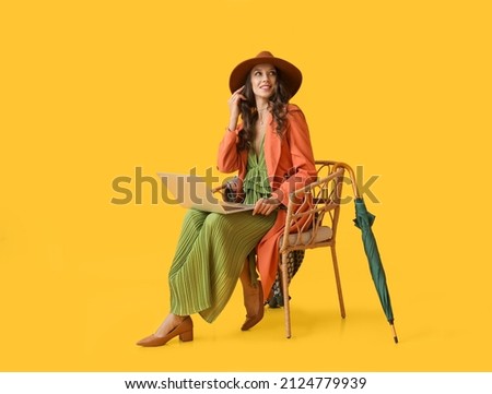 Young fashionable woman sitting in chair with laptop on yellow background