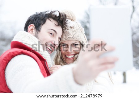 Happy couple in winter holiday taking tablet computer pictures