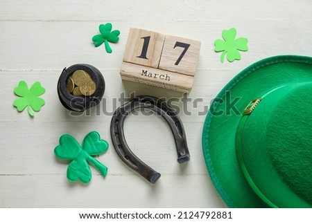 Leprechaun pot with golden coins, hat, horseshoe and calendar with date of St. Patrick's Day on white wooden background