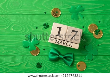 Top view photo of st patrick's day decorations shamrocks wooden cubes calendar 17 march clover shaped confetti green bow-tie and gold coins on isolated textured green wooden desk background