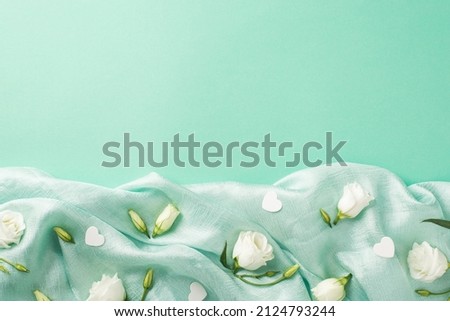 Top view photo of the amazing white eustomas with cute confetti in shape of hearts scattered on the folds of the textured pastel teal background empty space