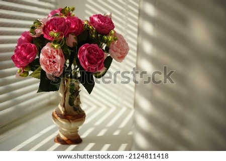 Pink peony flowers in vase on sunny windowsill.